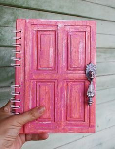 a hand holding a pink notebook with an open door