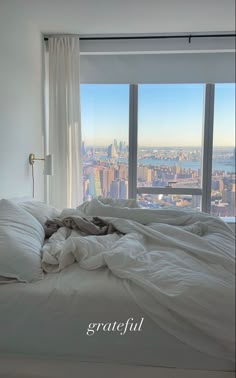 an unmade bed in front of a large window with the view of new york city