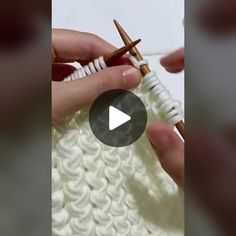 someone crocheting with yarn and knitting needles in the shape of a cross on a white surface