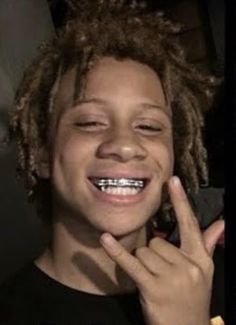 a young boy with dreadlocks smiles and holds his hand up to his face