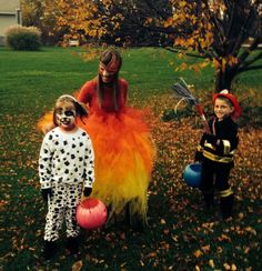 two children dressed up in costumes standing next to each other on the grass with fall leaves around them