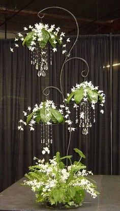 an arrangement of white flowers and greenery on a table in front of a black curtain