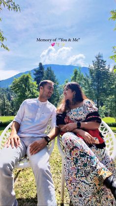 a man and woman sitting on top of a white chair next to each other in the grass