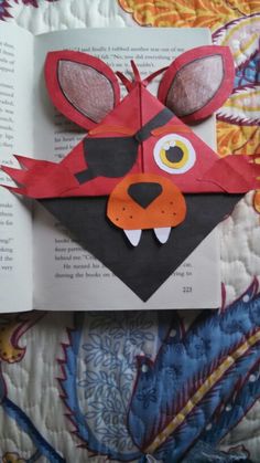 an animal made out of paper sitting on top of a bed next to a book