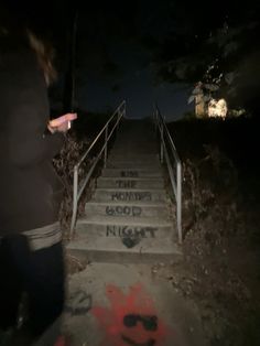 someone walking up some stairs at night with graffiti on the steps and handrails