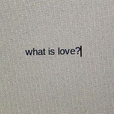 the word what is love written in black ink on a gray fabric textured background