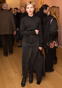 a woman standing in front of a group of people wearing black clothing and holding a handbag