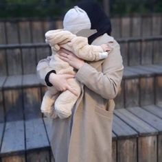 a woman holding a stuffed animal in her arms while wearing a hat and trench coat