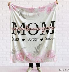 a woman holding up a pink and white blanket with the words mom written on it