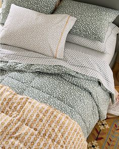 a bed with green and yellow comforters on it's headboard next to a rug