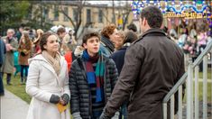 two people standing next to each other in front of a group of people on a sidewalk