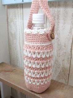 a pink and white crocheted bag hanging from a hook on a wooden wall