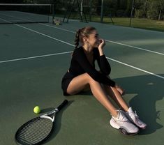 a woman sitting on the ground with a tennis racket and ball in her hand