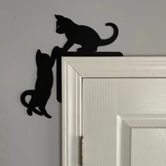 a black cat is climbing up the side of a door with its tail hanging down