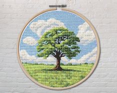 a cross stitch picture of a tree on a white brick wall with clouds in the background