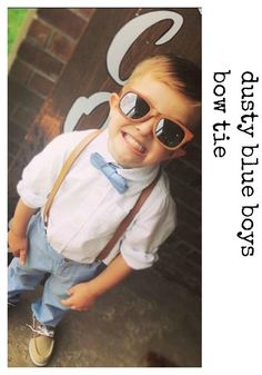 a young boy wearing sunglasses and suspenders standing in front of a brick wall