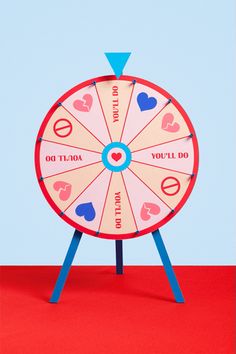 a spinning wheel with hearts on it sitting on top of a red table next to a blue wall