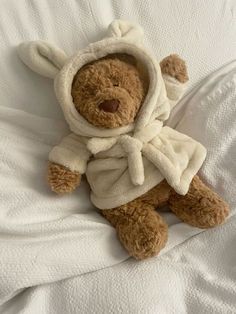 a teddy bear wearing a robe on top of a white bed sheet covered in blankets