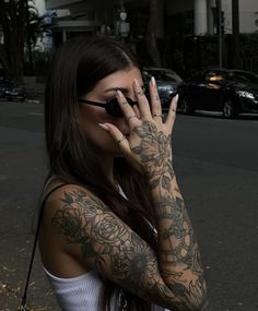 a woman with tattoos on her arm and hand covering her face while talking on the phone