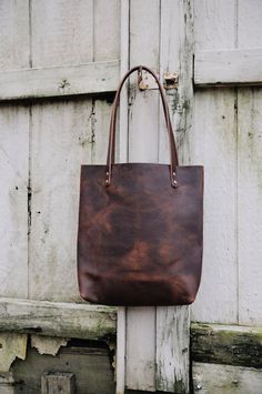 "Made out of super sturdy Kodiak leather, this tote will only look better with each wear. This leather is paired with a wonderful piece of Cowhide. Hang pocket on the inside, sturdy and thick leather straps. See Add on items here - Pocket, strap, zipper: http://etsy.me/2eCNuDk Choose tall or short, light or dark cowhide. Light will have mostly brown and white spots, dark will have mostly black and white spots. First picture is the SHORT tote, light cowhide, with button stud closure and cross bod Brown Leather Tote Bag, Brown Leather Purse, Cowhide Bag, Small Leather Bag, Brown Leather Totes, Large Leather Tote, Leather Laptop Bag, Handmade Leather Wallet, Brown Leather Bag