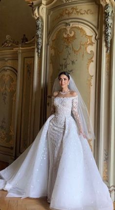 a woman in a white wedding dress standing next to a wall with gold trimmings