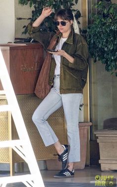 a woman in jeans and jacket standing next to a stair case with her hand on her head