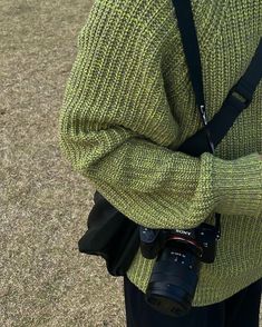 a person wearing a green sweater holding a camera in their hand while standing on the grass