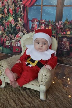 a baby dressed as santa claus sitting in a chair