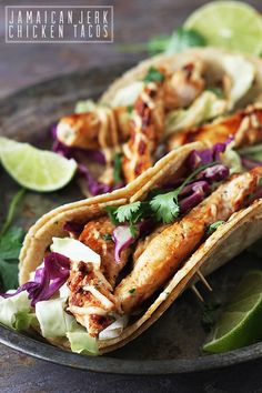 two chicken tacos on a plate with lime wedges