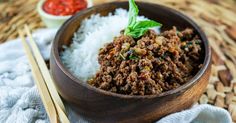 a wooden bowl filled with meat and rice next to chopsticks