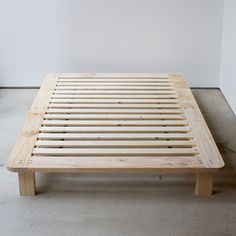 a wooden bed frame sitting on top of a cement floor next to a white wall