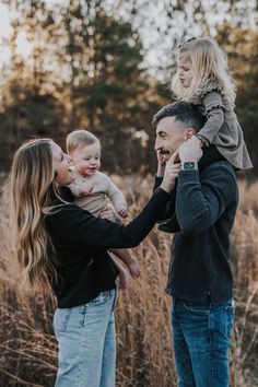 a man and woman holding a child in their arms while they stand in tall grass