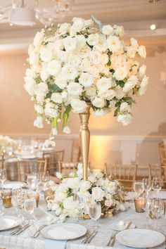 an elegant centerpiece with white flowers and greenery sits atop a table set for a formal dinner