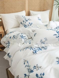 a bed with blue flowers on it and white linens in front of a wicker headboard