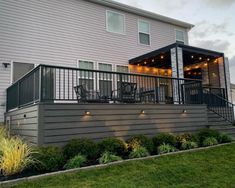 an outdoor deck with lights and chairs on the side of a house in front of a large white building