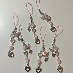 several charms are hanging from pink cords on a white surface, one has an angel and the other has hearts