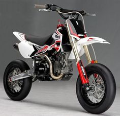 a red and white dirt bike parked on top of a cement floor next to a gray wall