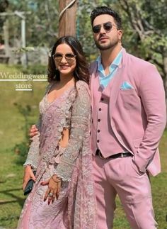 a man and woman standing next to each other in front of a tree wearing pink outfits