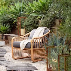 a wicker chair sitting in the middle of a garden with potted plants behind it