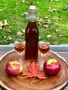 an apple cider and two glasses on a wooden plate with leaves next to it