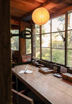 a wooden table sitting under a window next to a lamp