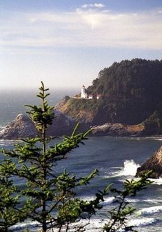 a lighthouse on top of a hill next to the ocean with trees in front of it