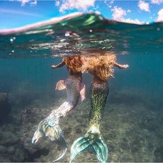 two mermaids are swimming in the ocean with their tails spread out and there is no image here to provide a caption for