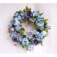 a wreath with blue flowers and green leaves on a white tablecloth, ready to be used as an ornament