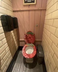 a red toilet sitting in a bathroom next to a trash can