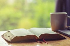 an open book sitting on top of a wooden table next to a laptop and coffee cup