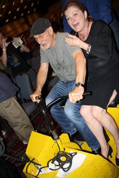 a man and woman riding on the back of a yellow bike in an arena with people watching