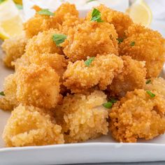 fried food on a white plate with lemon wedges