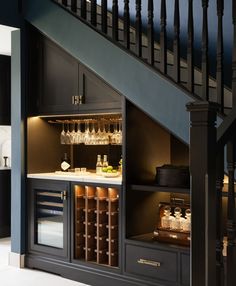 an open cabinet under the stairs with wine glasses and bottles on it, in front of a stair case