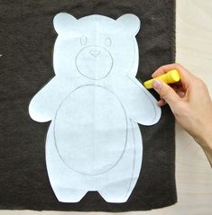 someone is cutting out a paper teddy bear on a piece of black fabric with a yellow marker